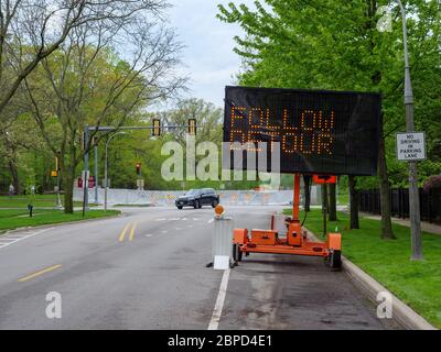 River Forest, Illinois, USA. Mai 2020. Elektronisches Umleitungsschild leitet den Verkehr von der Chicago Avenue Brücke über den des Plaines River weg. Die Straße war wegen Brückenarbeiten gesperrt worden, aber der Fluss überflutete nach heftigen Regenfällen, so dass eine temporäre Hochwasserbarriere gebaut werden musste, die im Hintergrund zu sehen war. Stockfoto