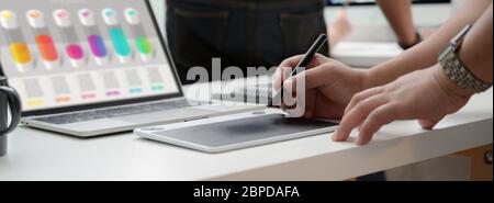 Kurzer Schnitt eines Grafikdesigners, der an einem Infografik-Projekt mit einem Tablet und einem Laptop arbeitet Stockfoto