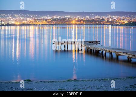 Leerer Angelpier bei Nacht mit der Stadt im Hintergrund mit Orange und blauem Grün Stockfoto