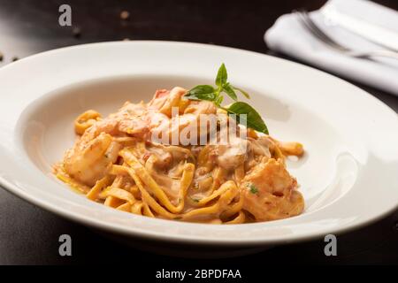 Pasta fetuccini mit Garnelen und Gewürzsauce auf einem weißen Teller Holztisch Stockfoto