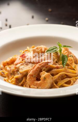 Pasta fetuccini mit Garnelen und Gewürzsauce auf einem weißen Teller Holztisch Stockfoto