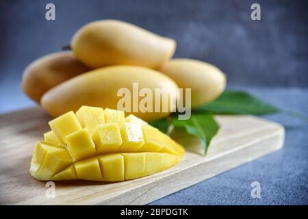 Mango-Scheibe mit frischer, reifer Mango und grünen Blättern auf einem Holz mit schwarzem Hintergrund. Tropische Früchte. Selektiver Fokus. Freier Platz für Ihren Text. Stockfoto