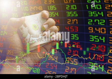 Börsenkonzept. Geschäftsmann Hand hält Thai Banknoten und Aktienmarkt Diagramm und Chart-Preis-Anzeige. Konzept Finanzanalyse mit thai b Stockfoto