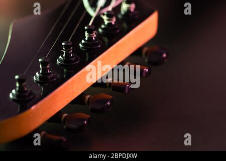 Closeup Stimmschlüssel auf der Kopfplatte der schwarzen E-Gitarre im dunklen Hintergrund und Morgenlicht. Kopierbereich rechts. Konzept der guten Erinnerung Stockfoto