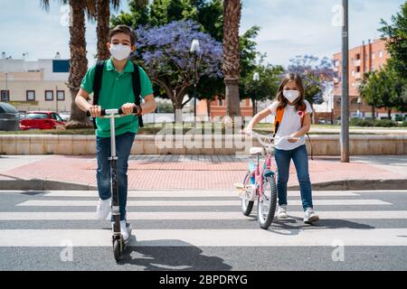 Junge und Mädchen tragen Masken und fahren einen Roller und Fahrrad auf der Straße Stockfoto