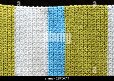 Fragment of crocheted fabric from green, blue and light blue threads close-up, top view. Abstract background. Hand made concept Stockfoto