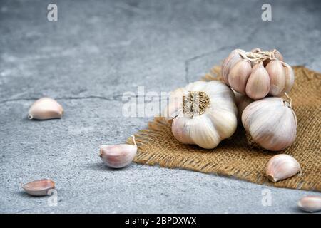 Bio-Knoblauch. Frische Knoblauchzehen und Knoblauchzwiebel auf Jute auf dunklem Hintergrund mit Knoblauchhaufen oder Gewürzen. Ausgewählter Fokus. Konzept der Gewürze für hea Stockfoto