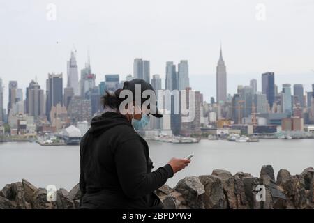 New York, USA. Mai 2020. Eine Frau mit Gesichtsmaske geht in der Nähe des Hamilton Parks mit der Skyline von Manhattan im Hintergrund in Weehawken von New Jersey, USA, am 18. Mai 2020. Die Anzahl der COVID-19-Fälle in den Vereinigten Staaten überstieg 1.5 Millionen am Montag, erreichte 1,500,753 von 16:03 Uhr (2003 GMT), nach dem Center for Systems Science and Engineering (CSSE) an der Johns Hopkins University. Die nationale Todesrate von COVID-19 stieg laut CSSE auf 90,312. Kredit: Wang Ying/Xinhua/Alamy Live News Stockfoto