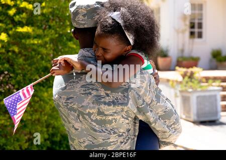 Afroamerikanischer Soldat, der seine Tochter mit einer US-Flagge in den Armen hält Stockfoto