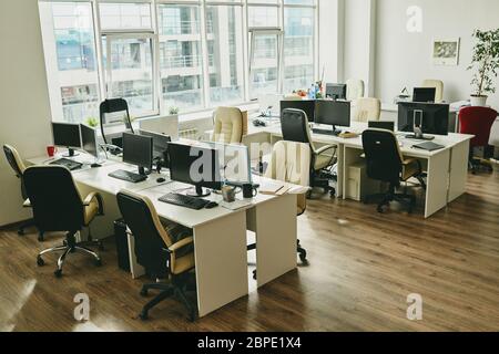 Niemand in modernen Büro mit großen Fenster und Schreibtisch mit Computern und Tassen, covid-19 Konzept Stockfoto