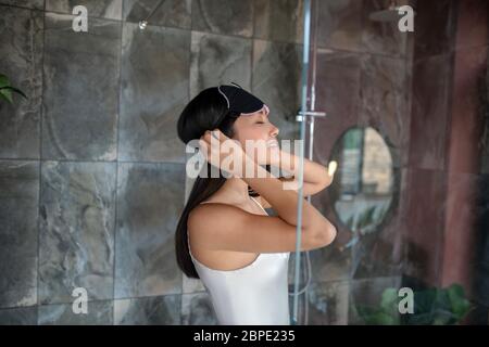 Brunette weibliche Fixierung ihrer Schlafmaske, in der Dusche stehend Stockfoto