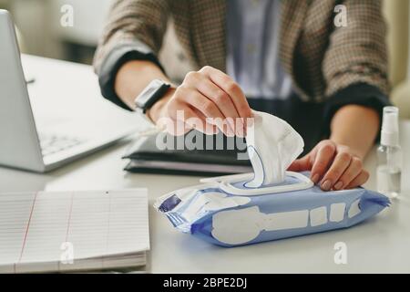 Nahaufnahme einer nicht erkennbaren Frau, die am Schreibtisch sitzt und mit einem feuchten Tuch am Arbeitsplatz desinfiziert wird Stockfoto