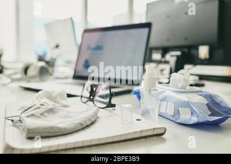 Nahaufnahme der Verpackung mit nassem Wischtuch, Brillen, Desinfektionsflasche mit Spender und Stoffmaske auf Notizblock auf dem Schreibtisch Stockfoto