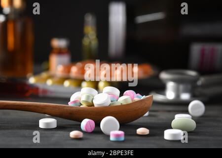 Verschiedene pharmazeutische Medizin Pillen, Tabletten und Kapseln in Holzlöffel auf schwarzem Holzgrund. Medizinische Konzepte. Minimalistisches abstraktes CO Stockfoto