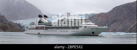 Panorama von Seabourn Sojourn Kreuzfahrtschiff driftet mit einem massiven Gletscher und Bergen dahinter in Alaska, USA Stockfoto