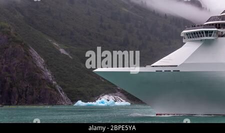 Kreuzfahrtschiff Segeln in Alaska unter Eisbergen. Schiffsbogen mit Bergen und Wolken im Hintergrund. Stockfoto