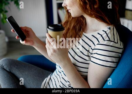 Frau sitzt mit einem Telefon und einer Tasse Kaffee Stockfoto