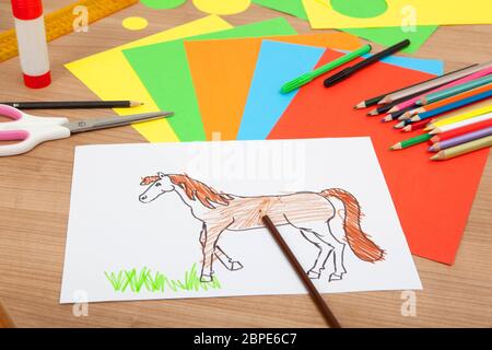 von einem Kind gemalt Pony auf einem weißen Papier, liegen auf einem Tisch mit Bleistiften und bunten Karton Stockfoto