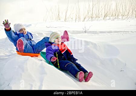 Zwei kleine Mädchen auf einem Schlitten schieben bergab auf Schnee im winter Stockfoto