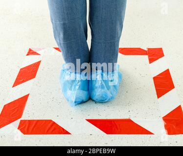 Frau stehen in der Linie halten soziale Distanz tragen Überschuhe, medizinische Schuhüberzüge im Laden, Supermarkt, Krankenhaus. Menschen, die hinter einer Warnung stehen Stockfoto