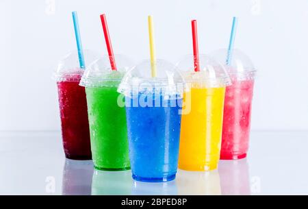 Stillleben Profil von gefrorenen Früchten Slush Granita Getränke in Kunststoff Take Away Tassen mit Deckel und Trinkhalme auf reflektierende Oberfläche in Fron angeordnet Stockfoto