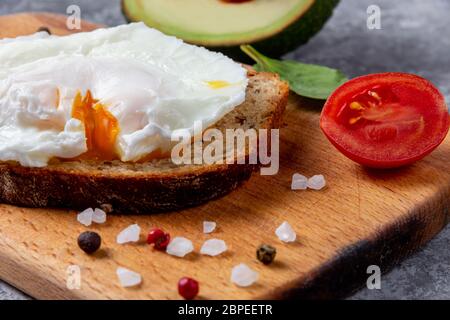 Pochiertes Ei mit Avocado auf Vollkornbrot nahe an Rotkirsche und Spinat auf Holzbrett Stockfoto