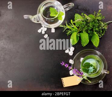 Frisch gebrühter Pfefferminztee mit frischen pflanzlichen Zutaten und Blumen neben in einer Glasbecher und Teekanne für ein erfrischendes gesundes Getränk, Overhead V Stockfoto