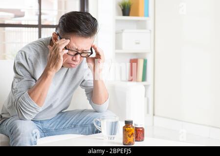 Porträt der 50er Jahre reifen asiatischen Mann mit Kopfschmerzen, auf Sofa sitzen, zu Hause, Zuhause Leben Lifestyle. Stockfoto