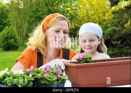 Junge Frau und kleines Mädchen im Garten im Frühjahr, Pflanzen Blumen Setzlinge, lächelnde Mutter und ihr glückliches Kind im Garten arbeiten Stockfoto