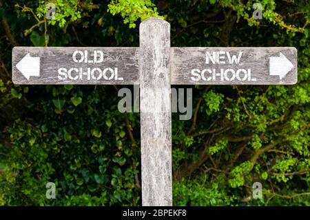 Hölzerne Wegweiser mit zwei entgegengesetzten Pfeilen über grüne Blätter Hintergrund. Alte Schule, NEUE SCHULE Wegweiser, Wahl Konzept Bild Stockfoto