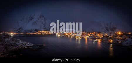 Nachtpanorama des berühmten Fischerdorfes reine, lofoten in schweren Schneesturm. Blizzard und starker Wind am Hafen - im Hintergrund dunkle Berge mit einer bedeckten w Stockfoto