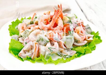 Salat mit Garnelen, Avocado, Tomaten und Mayonnaise auf den Salat auf dem Teller, Serviette, Gabel auf Holzbrett Hintergrund Stockfoto