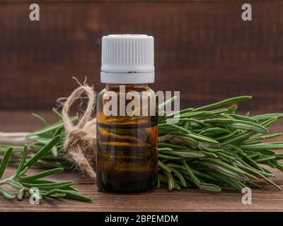 Ätherisches Rosmarinöl in dunklen Glasflasche und frischem Rosmarin auf dunklem Holz mit Textfreiraum Stockfoto