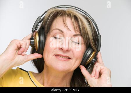 Kopf-und-Schulter-Ansicht einer Frau mittleren verändert, mit geschlossenen Augen und Kopfhörern vor weißem Hintergrund. Stockfoto
