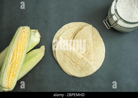 Frisch gebackenes Tortilla-Brot, Maismehl im Glas und grüne Maiskolben auf Beton, Stein Hintergrund. Köstliche, traditionelle, gesunde Lebensmittel. Draufsicht, flach Stockfoto