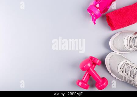 Fitness-Konzept flach auf grauem Hintergrund mit Sneakers, rosa Handtuch, Hanteln und Wasserflasche, flach Ley Copy Raum Stockfoto