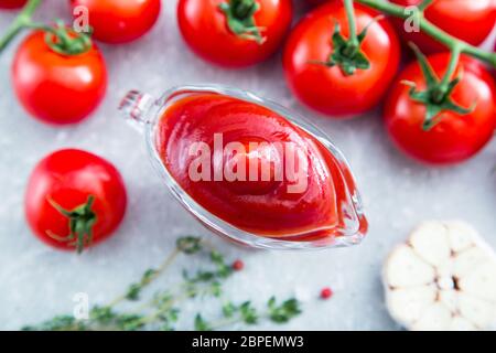 Tomatenketchup-Sauce mit Knoblauch, Gewürzen und Kräutern mit Kirschtomaten in einer Glasschüssel auf Steintisch, selektiver Fokus. Stockfoto