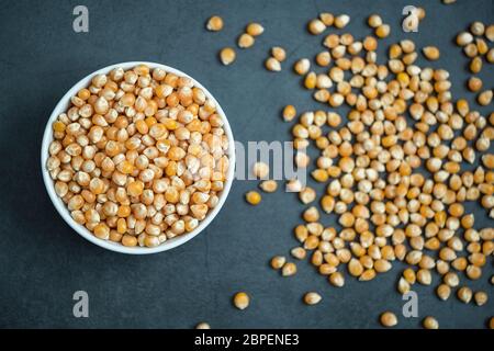 Roh Mais-Kern in Schüssel und verteilt um auf Stein, Beton Hintergrund. Flache Lay-Komposition. Gesunde, biologische und leckere Speisen. Stockfoto