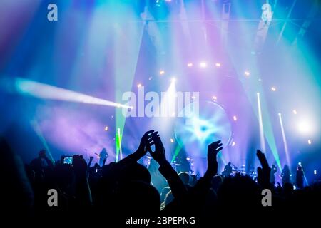 Viele Menschen genießen, Konzert, die Band auf der Bühne in der hellen blauen Licht führt, Leute, Musik, Tanzen mit erhobenen Händen und klatschen, activ Stockfoto