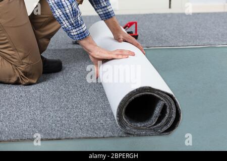 Junge männliche Heimwerker Rolling Teppich auf dem Boden zu Hause Stockfoto