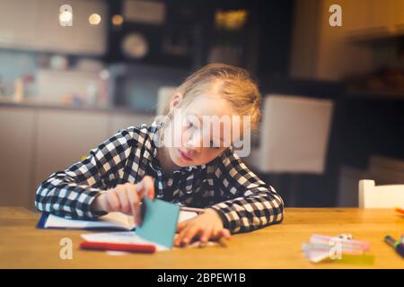 Schöne, blonde Mädchen am Tisch sitzt und macht Hausaufgaben zu Hause Stockfoto