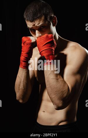 Boxer-Kämpfer posieren in selbstbewusster defensiver Haltung mit Händen in banndages oben auf schwarzem Hintergrund Stockfoto