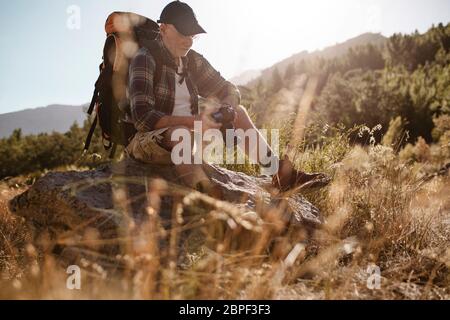 Wanderer, die Bilder auf der Digitalkamera während der Wanderung betrachten. Älterer Mann, der eine Pause auf einer Wanderung zum Betrachen von Fotos nimmt. Stockfoto