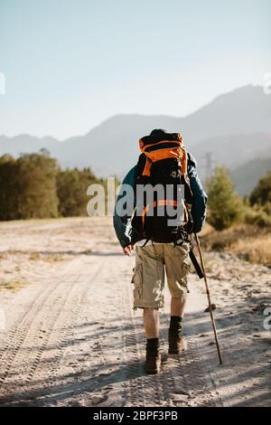 Rückansicht des Menschen mit Rucksack, der über einen Bergpfad geht. Männliche Wanderung durch Bergweg. Stockfoto