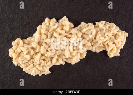 Traditionelle slowakische Essen bryndzove halusky in der Form der Slowakischen Republik auf schwarzem Hintergrund von oben. Kartoffelklöße. Stockfoto