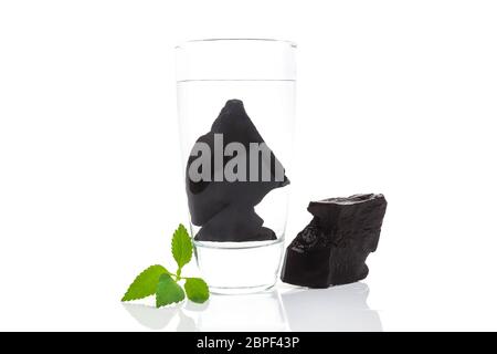 Reinigen von Wasser mit shungite Steine. Glas Wasser mit shungite Steine isoliert auf Weiss. Entfernen der Giftstoffe und organische Stoffe aus dem Wasser. Stockfoto