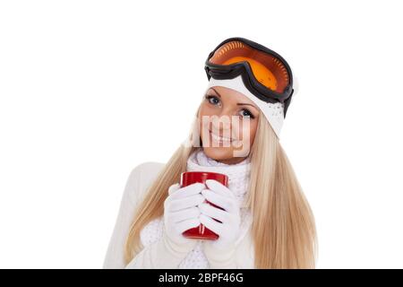 Junge Frau in Skibrillen und warme Winterkleidung mit roten Tasse steht auf einem weißen Hintergrund. Wintersport. Stockfoto