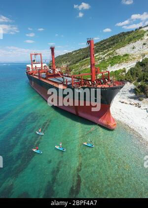 Kabardinka, Russland - 05. Juli 2019 Trockenfrachtschiff RIO verließ die Küste. Gruppe von Personen Paddeln auf SUP-Bord in der Nähe von Schiff. Stockfoto