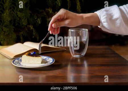 Frau Hand mit Gabel Essen Scheibe Käsekuchen mit Tasse Kaffee Ion der Tisch Stockfoto