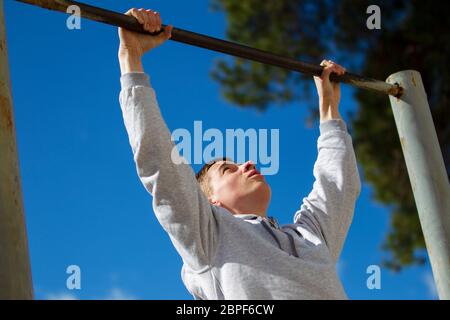 Der Junge zieht sich auf der horizontalen Stange auf der Straße hoch. Ein junger Mann macht Übungen. Stockfoto